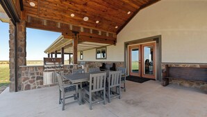 Een terras buiten, met een stenen muur, een barbecue en een houten tafel met stoelen.