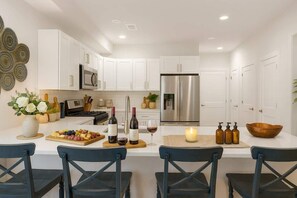 Una cocina moderna con armarios blancos, electrodomésticos de acero inoxidable, una isla central con asientos y un elemento decorativo en la pared.