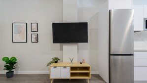 Une cuisine moderne dotée d’un téléviseur encastré, d’un réfrigérateur en acier inoxydable et d’un meuble en bois agrémenté d’objets décoratifs.