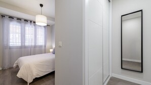 Une chambre à coucher avec un lit, une table de chevet, une lampe et un grand miroir au mur.
