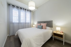 Et soveværelse med seng, to sengeborde, en natbord, et vindue med gardiner og en hængende lampe.