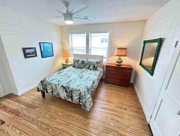 A bedroom with a bed, a nightstand, a lamp, a ceiling fan, and a window.
