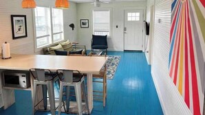 Une pièce avec une table en bois, des chaises, un canapé et un mur rayé aux couleurs vives.