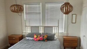 A bedroom with a bed, two nightstands, a ceiling fan, and a window with blinds. - Point Break Historic Beach Cottage (Carolina Beach)