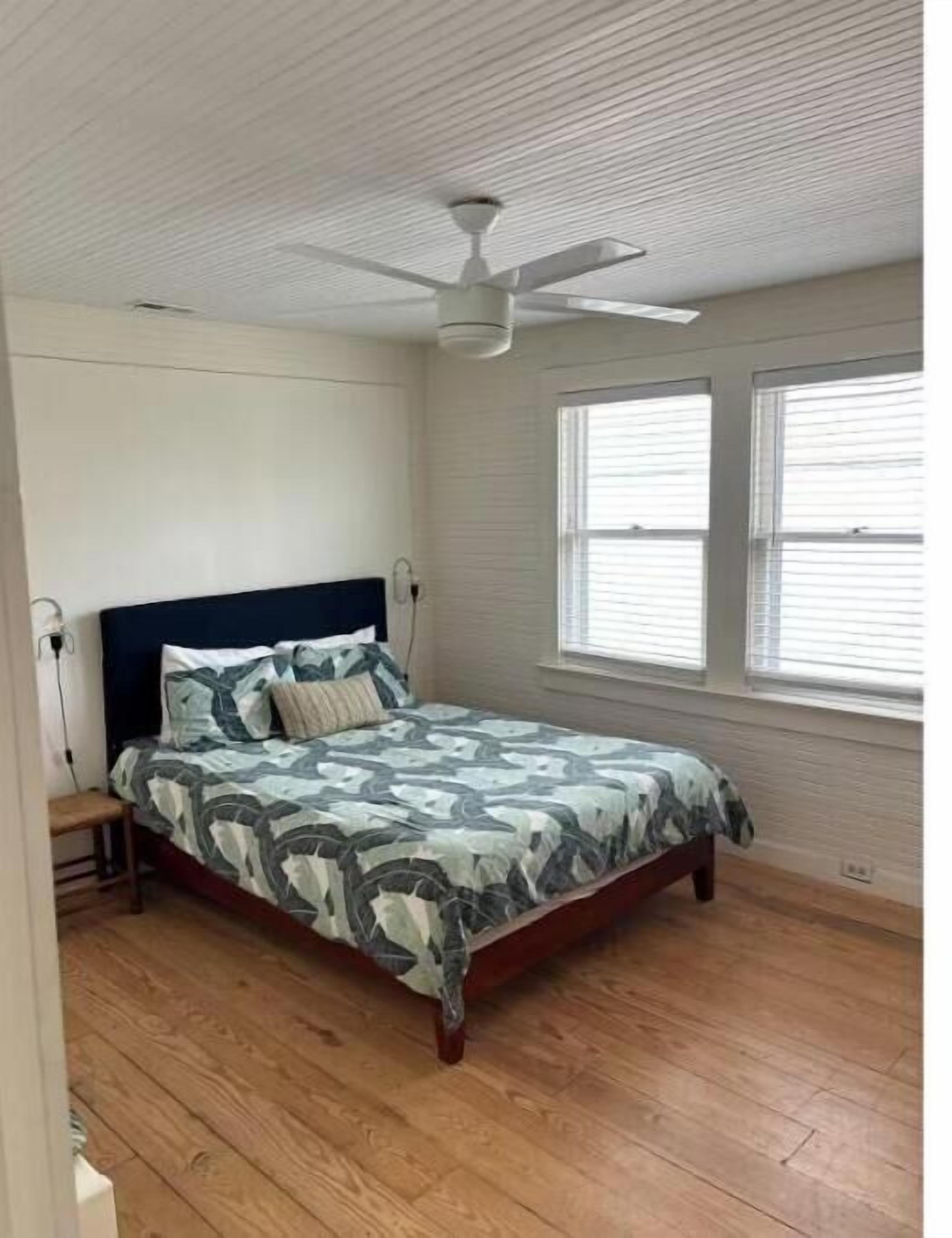 Un dormitorio con cama, ventilador de techo y ventana con persianas.