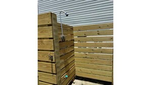 A wooden outdoor shower enclosure with a metal showerhead.