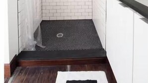 A shower with a white brick wall, a black shower mat, and a wooden floor. - Two Modern Containers-walk to the beach-Two blocks to the beach-Pet Friendly (Carolina Beach)