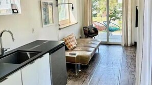 A modern kitchen with a black countertop and white cabinets, a dining area with a brown leather sofa and a small table, and a sliding glass door leading to a balcony with a chair. - Two Modern Containers-walk to the beach-Two blocks to the beach-Pet Friendly (Carolina Beach)