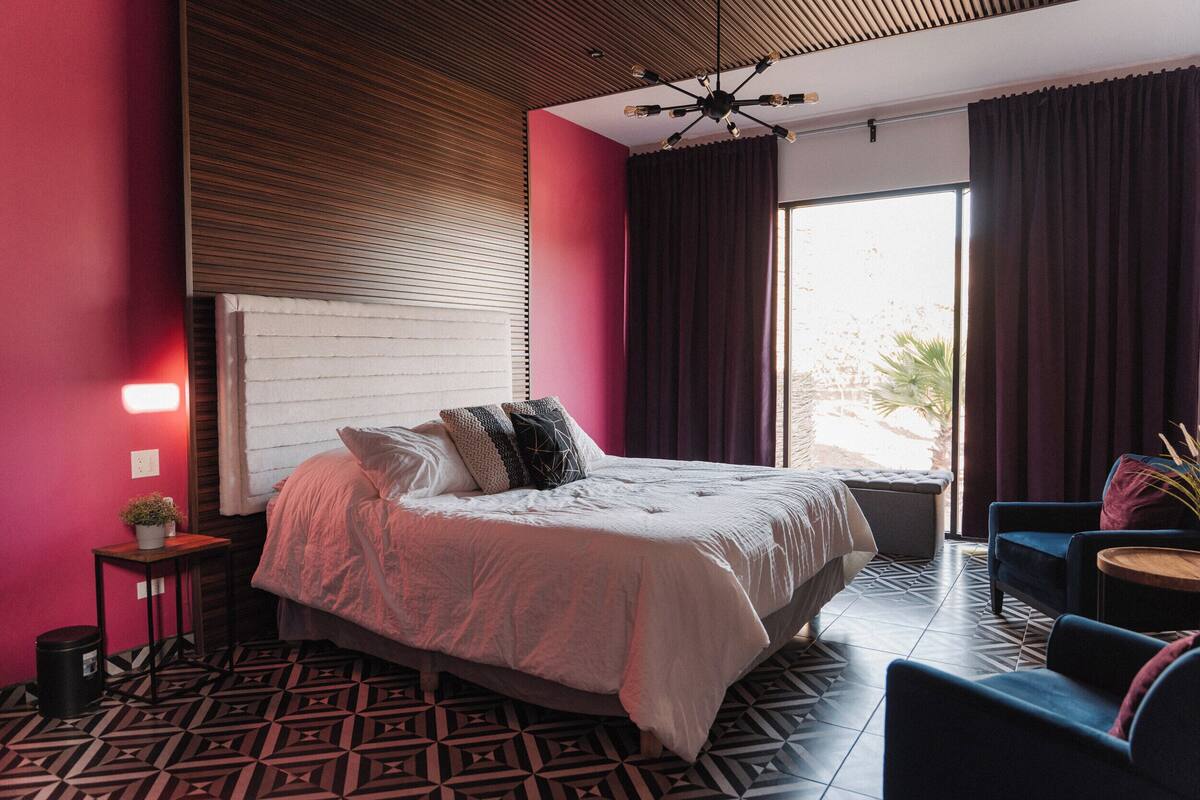 Een moderne slaapkamer met een groot bed, een klein tafeltje, een stoel en een raam met gordijnen.