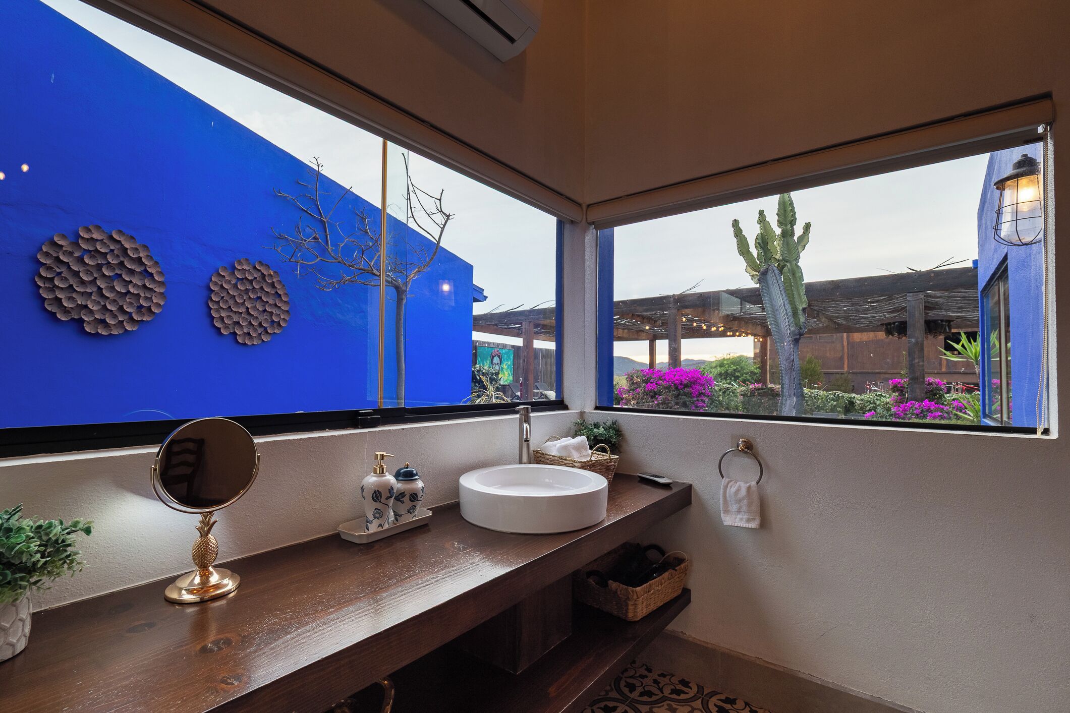 Un baño con un ventanal grande, un lavamanos redondo, un espejo y decoración en las paredes.