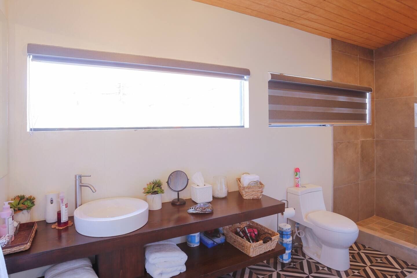 A modern bathroom with a large window, a sink, a mirror, a toilet, and a shower area.