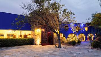 Un edificio con un patio empedrado de piedra, un árbol y fachada azul con arcos iluminados.
