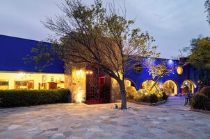 Un edificio con un patio empedrado de piedra, un árbol y fachada azul con arcos iluminados.