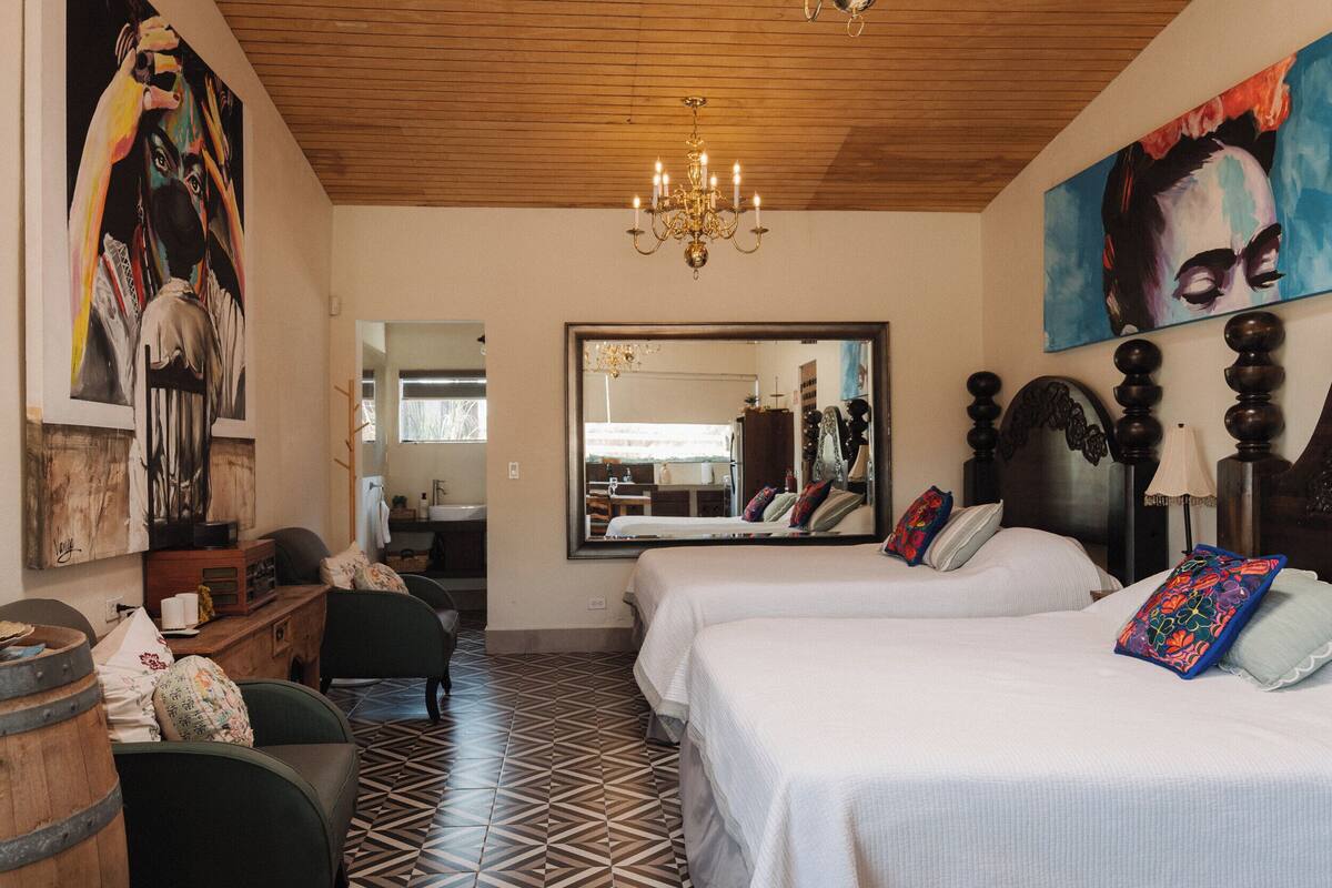 Een hotelkamer met twee bedden, een houten plafond, een kroonluchter en kunstwerken aan de muren.