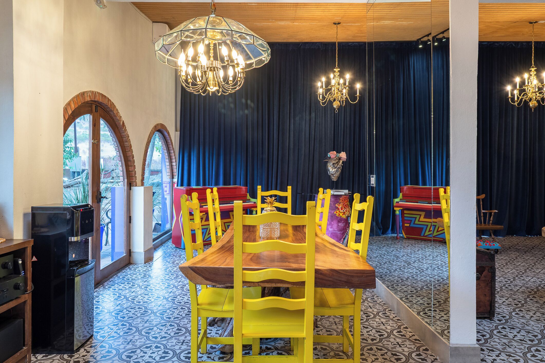 Un coin repas avec une table en bois et des chaises jaunes, un réfrigérateur noir et un rideau bleu en arrière-plan.