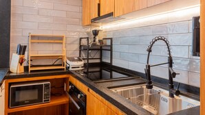 A compact kitchen with wooden cabinets, a black countertop, a stainless steel sink, and a microwave.