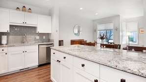 A modern kitchen with white cabinets, a granite countertop, and a dining area with wooden furniture. - Eaglewood 21 Sunriver with Pool,Tennis and Hot Tub (Sunriver)