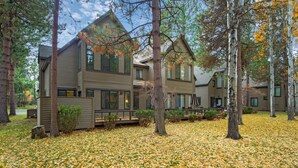 A two-story house with a deck and a covered patio area, surrounded by trees and a leaf-covered ground. - Eaglewood 21 Sunriver with Pool,Tennis and Hot Tub (Sunriver)