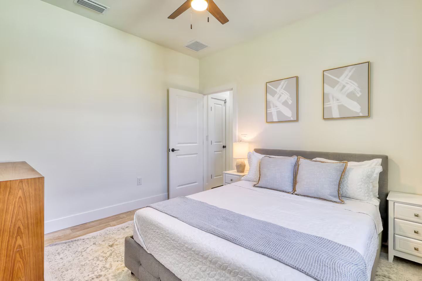 Ein Schlafzimmer mit einem Bett, Nachttischen, einem Deckenventilator und zwei gerahmten Bildern an der Wand.