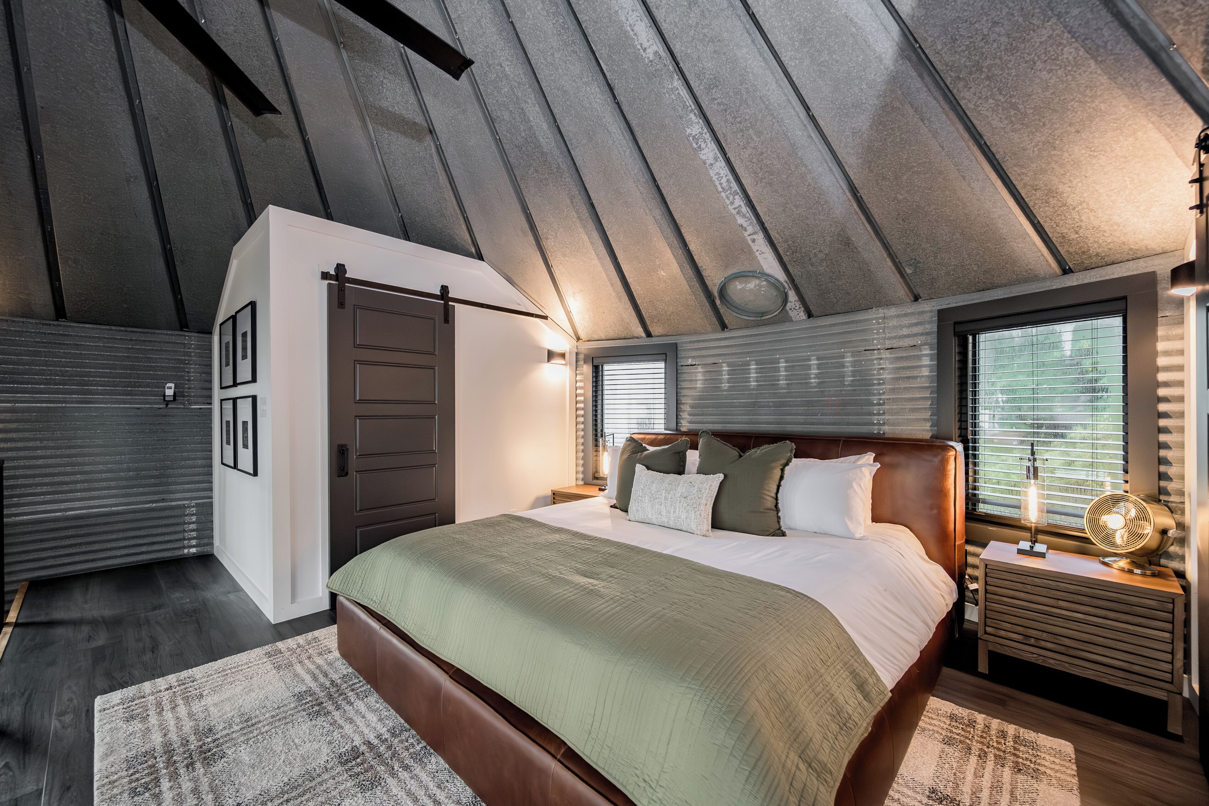 Un dormitorio con una cama grande, un cabecero de madera, una mesita de noche con lámpara y una ventana con persianas.