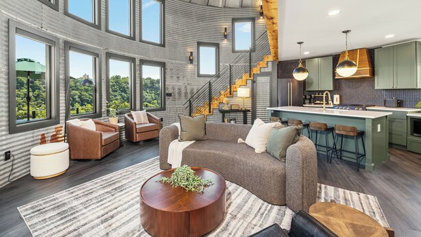 A spacious living area with a large sofa, a coffee table, and a staircase leading to a kitchen area. - Luxe Silo w/ River Views <.5 mi to Downtown (Lynchburg)