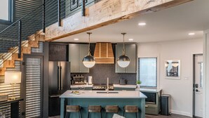 A modern kitchen with a central island, bar stools, and a staircase leading to an upper level. - Luxe Silo w/ River Views <.5 mi to Downtown (Lynchburg)