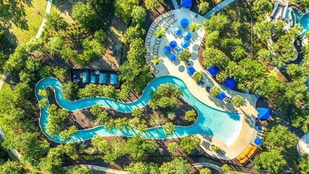 Vista aerea di un resort con piscina tortuosa, aree relax e un edificio separato con piscina.
