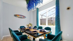 Un'area pranzo con un tavolo apparecchiato per sei persone, sedie color petrolio e una pianta decorativa pensile blu.