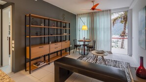 A modern living room with a large bookshelf, a dining area, and a balcony with a view. - House overlooking Rodrigo de Freitas Lagoon | VR2 (Rio de Janeiro)