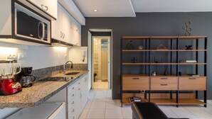 A modern kitchen with a built-in microwave, a coffee maker, and a blender. There is a wooden cabinet with multiple drawers and a black bench in the living area. - House overlooking Rodrigo de Freitas Lagoon | VR2 (Rio de Janeiro)