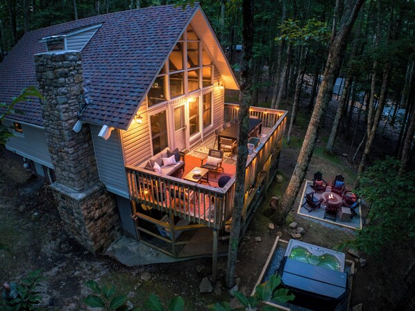 Une cabane avec une cheminée en pierre, une terrasse avec des sièges d’extérieur et un jacuzzi.