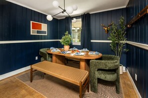 Un coin repas avec une table en bois dressée pour quatre personnes, entourée de chaises rembourrées, d’un banc et d’une plante en pot.