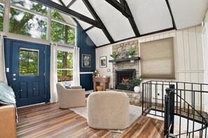 A room with a fireplace, wooden flooring, a blue door, and a staircase with a black railing.
