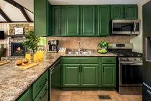 A kitchen with green cabinets, a stone fireplace, a stainless steel stove, and a microwave.