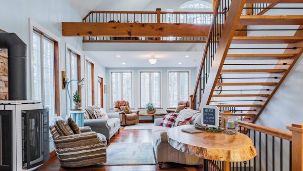 A spacious living area with a fireplace, wooden staircase, and a dining table with a sign. - Lake House On Sweet Arrow Lake (Pine Grove)