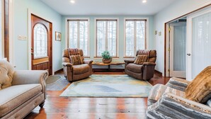 A cozy living room with a large window, two leather armchairs, a sofa, and a patterned rug. - Lake House On Sweet Arrow Lake (Pine Grove)