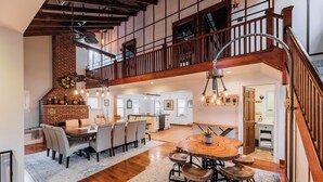 A spacious kitchen with a brick wall, wooden ceiling beams, and a dining area with a round wooden table and bar stools. - Lake House On Sweet Arrow Lake (Pine Grove)