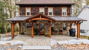 A two-story house with a stone facade, a covered porch, and a grill area. - Lake House On Sweet Arrow Lake (Pine Grove)
