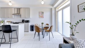 Une cuisine moderne avec des meubles blancs, un coin repas doté d’une table en verre et une grande fenêtre laissant entrer la lumière naturelle.