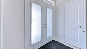 Un couloir doté d’une porte à deux vantaux et d’une porte simple, toutes deux pourvues de cadres blancs et de panneaux de verre.