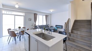 Une cuisine moderne avec un îlot central, un coin repas avec des chaises, un canapé et un escalier.