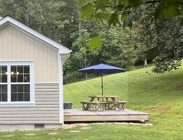 A small wooden structure with a window and a deck area with a picnic table and umbrella.