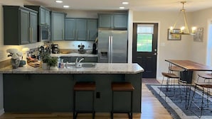 A kitchen with a central island, bar stools, a dining table with chairs, and a chandelier.