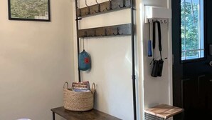A room with a metal rack with hooks, a basket, a small table, a trash can, and a window with blinds.