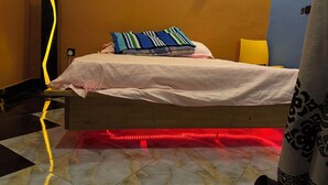 Ett sovrum med en säng, kuddar, ett sängbord, en lampa och en röd LED-ljuslist under sängen.