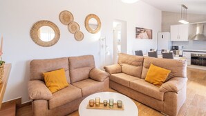 Un salon moderne avec deux canapés et une table basse, une cuisine en arrière-plan et des éléments décoratifs en forme d’œuvres d’art murales tissées.