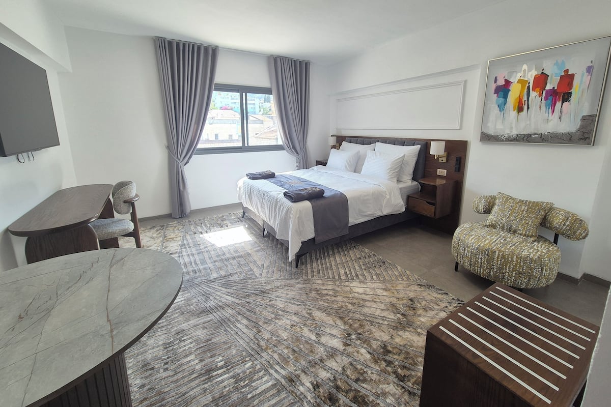Una habitación de hotel con una cama, un escritorio, una silla, una alfombra y un cuadro en la pared.