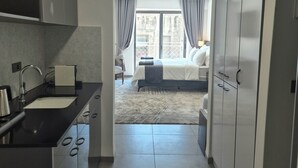 Une chambre d’hôtel moderne dotée d’un coin cuisine, d’un grand lit et offrant une vue sur le paysage urbain par la fenêtre.