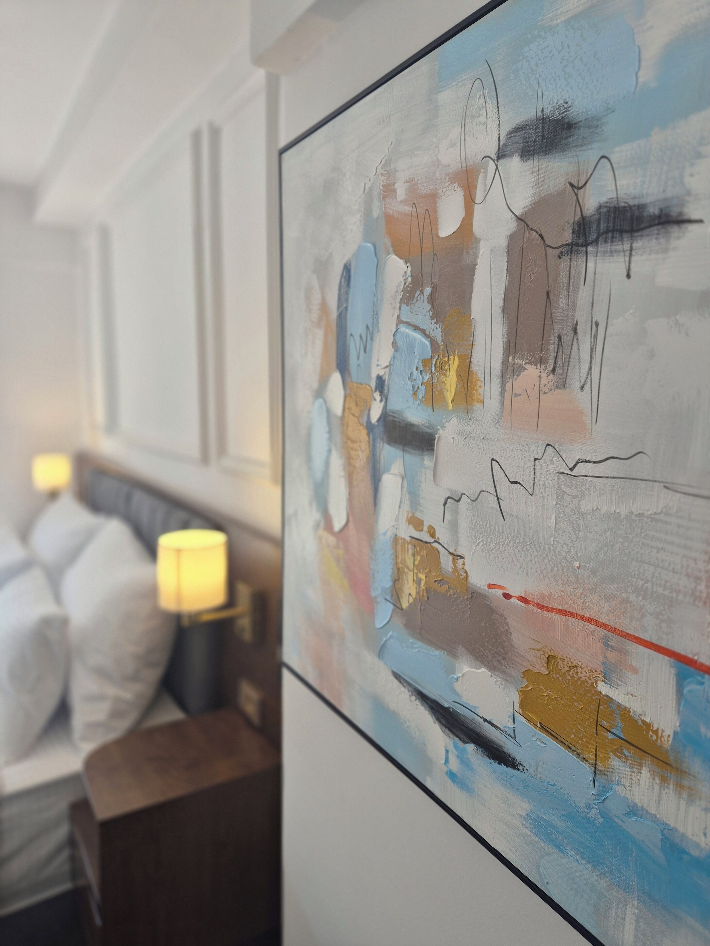 Un salon moderne avec un grand tableau abstrait accroché au mur, un canapé avec des coussins et une table d’appoint sur laquelle se trouve une lampe.