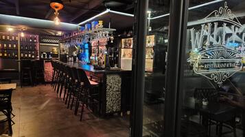 A bar area with a counter, stools, and shelves of bottles.